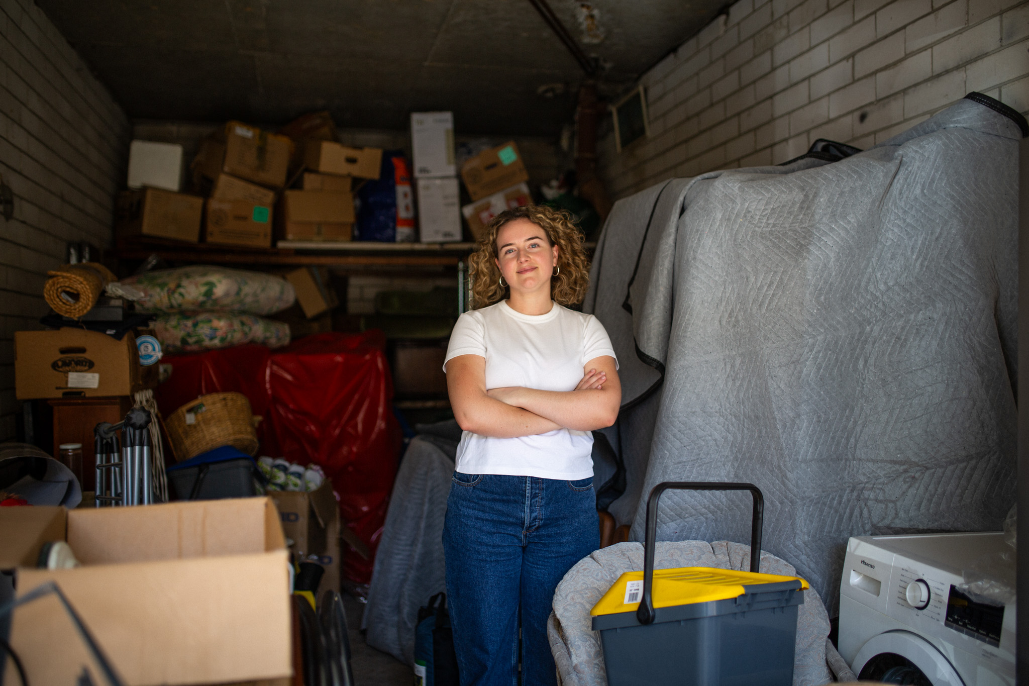 Sarah stands with her arms folded inside her parents' garage filled with her belongings